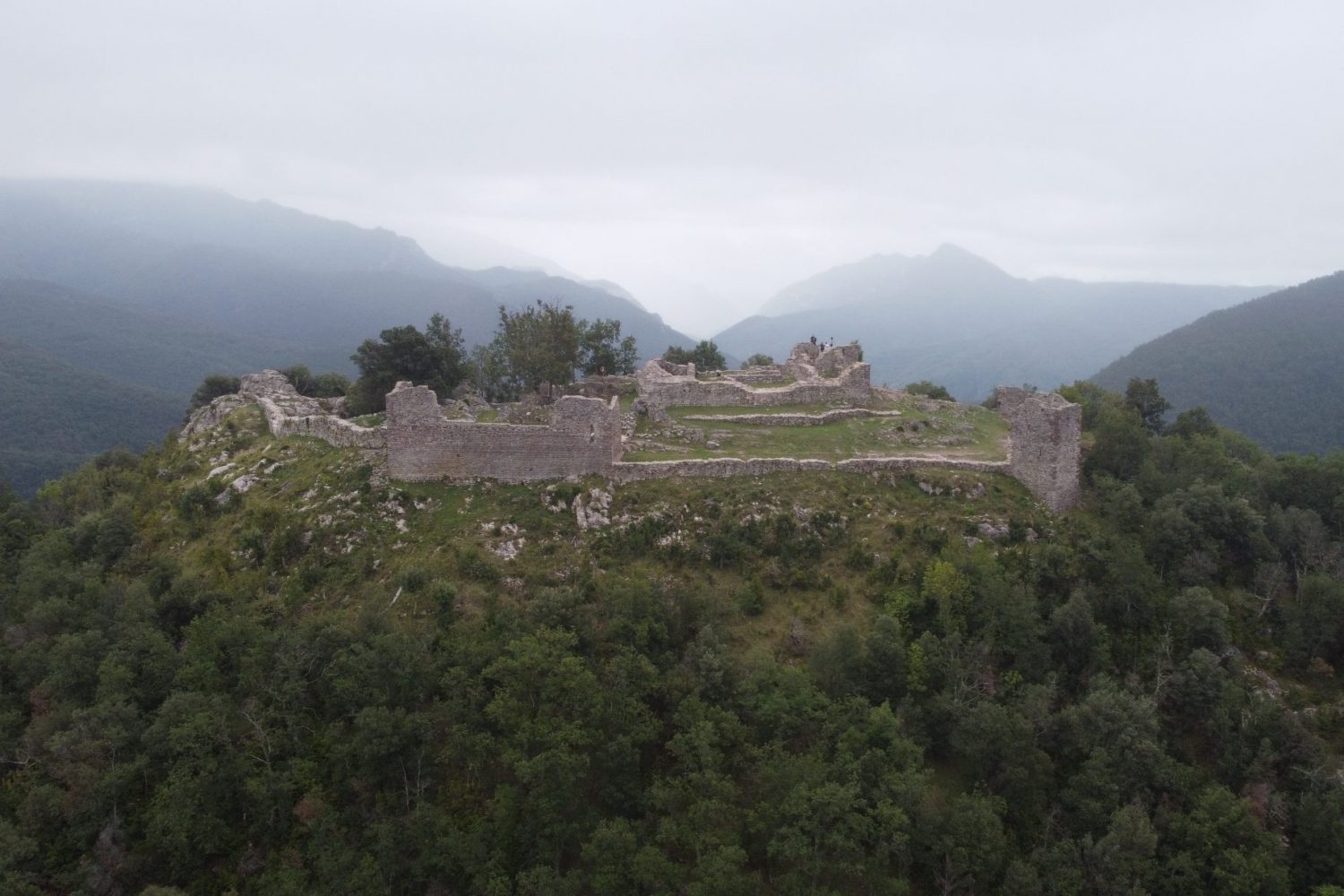 Ruïnes d’una fortificació de pedra sobre un turó envoltat de muntanyes.