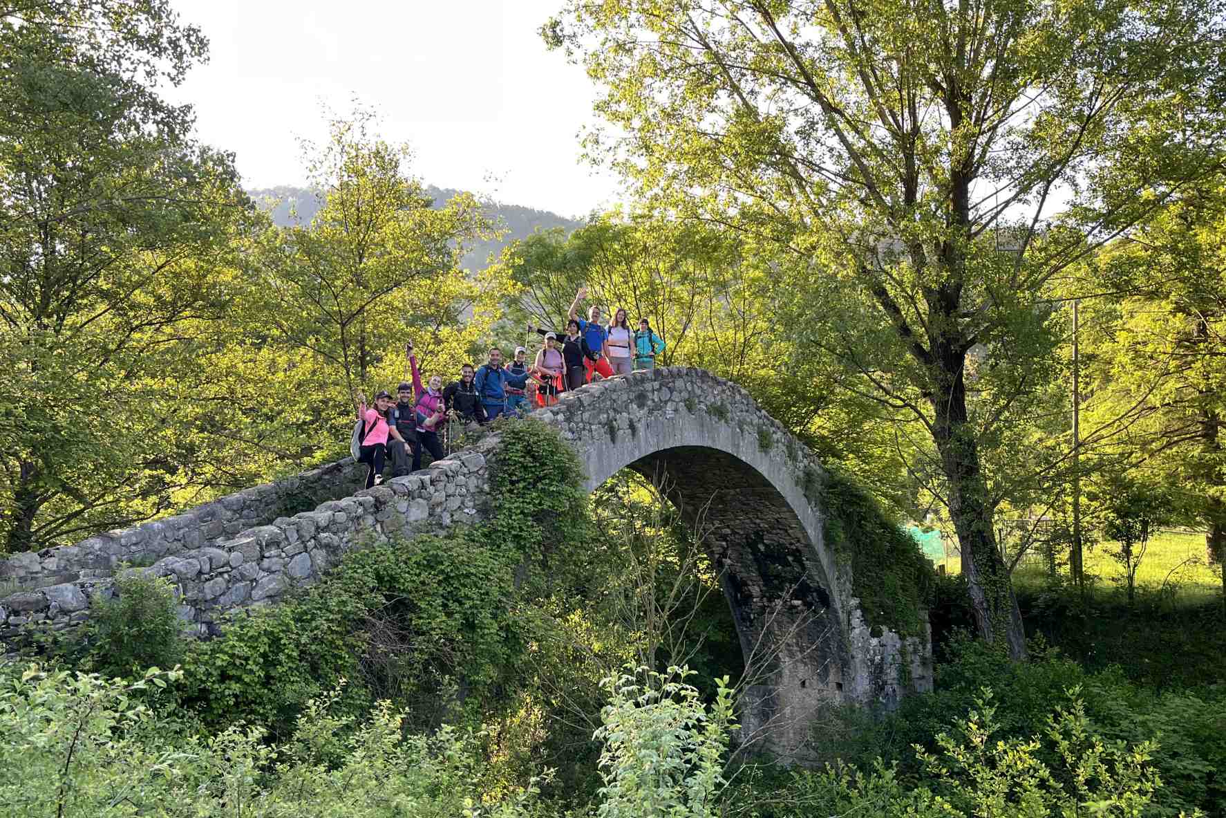 Grup aturat sobre un pont de pedra envoltat d’un bosc frondós.