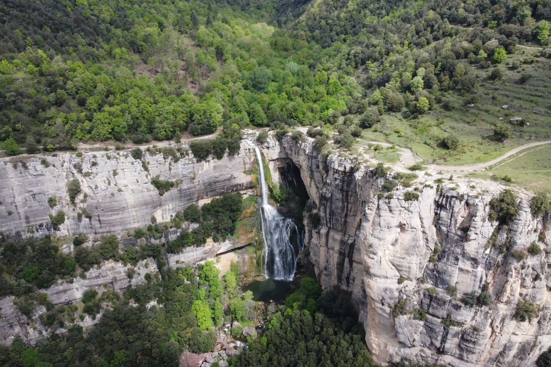Vista aèria d’un salt d’aigua que cau entre grans cingleres i bosc.